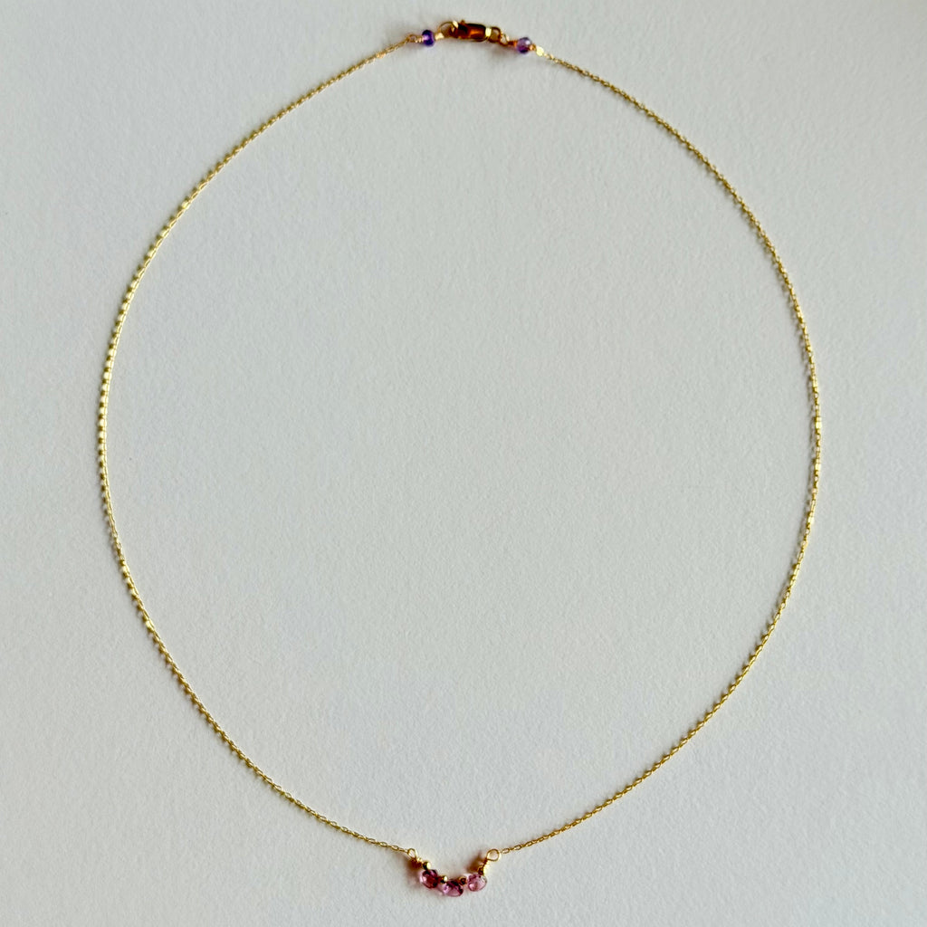 Gold necklace with small red beads on a light gray background
