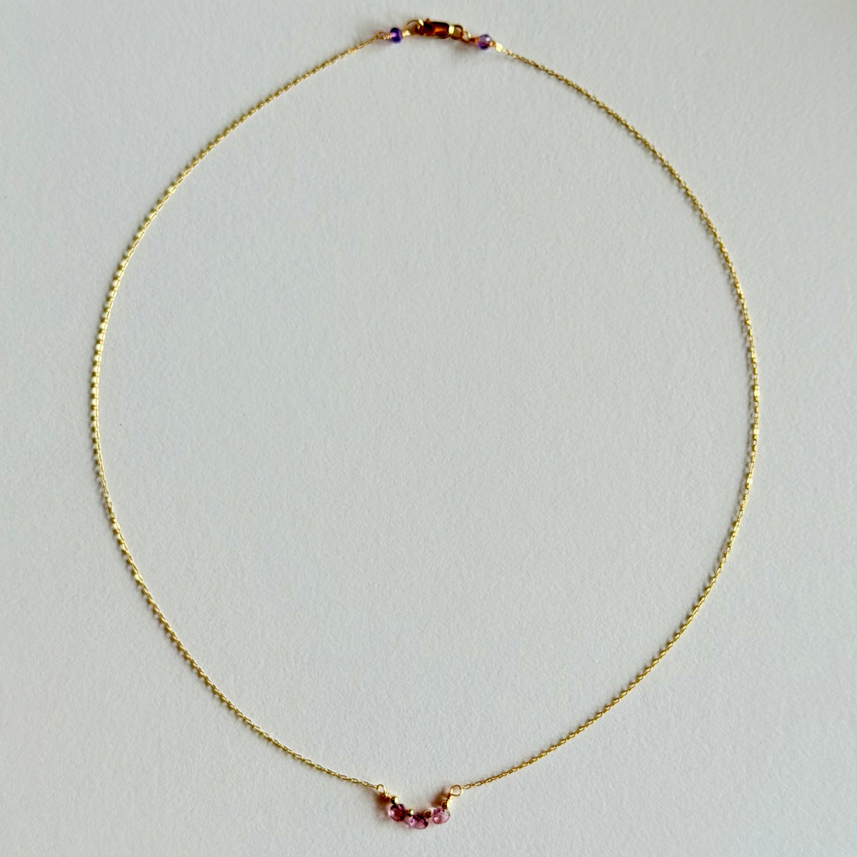 Gold necklace with small red beads on a light gray background