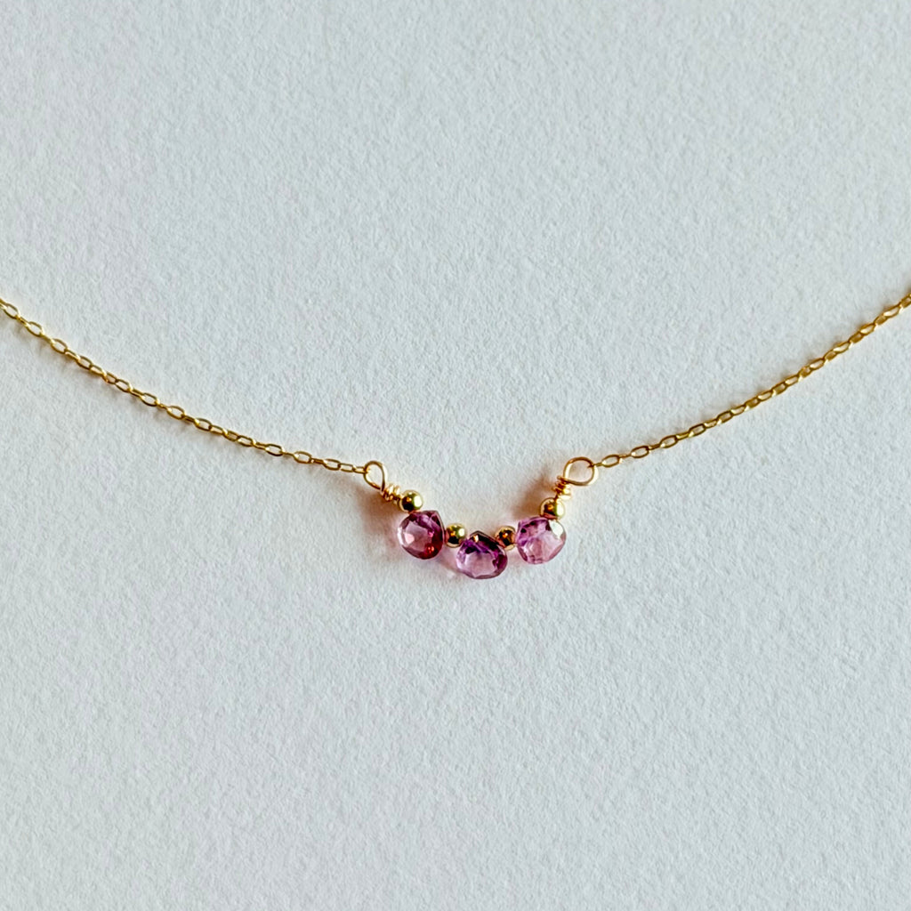 Delicate gold necklace with three small gemstones on a light gray background