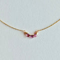 Delicate gold necklace with three small gemstones on a light gray background