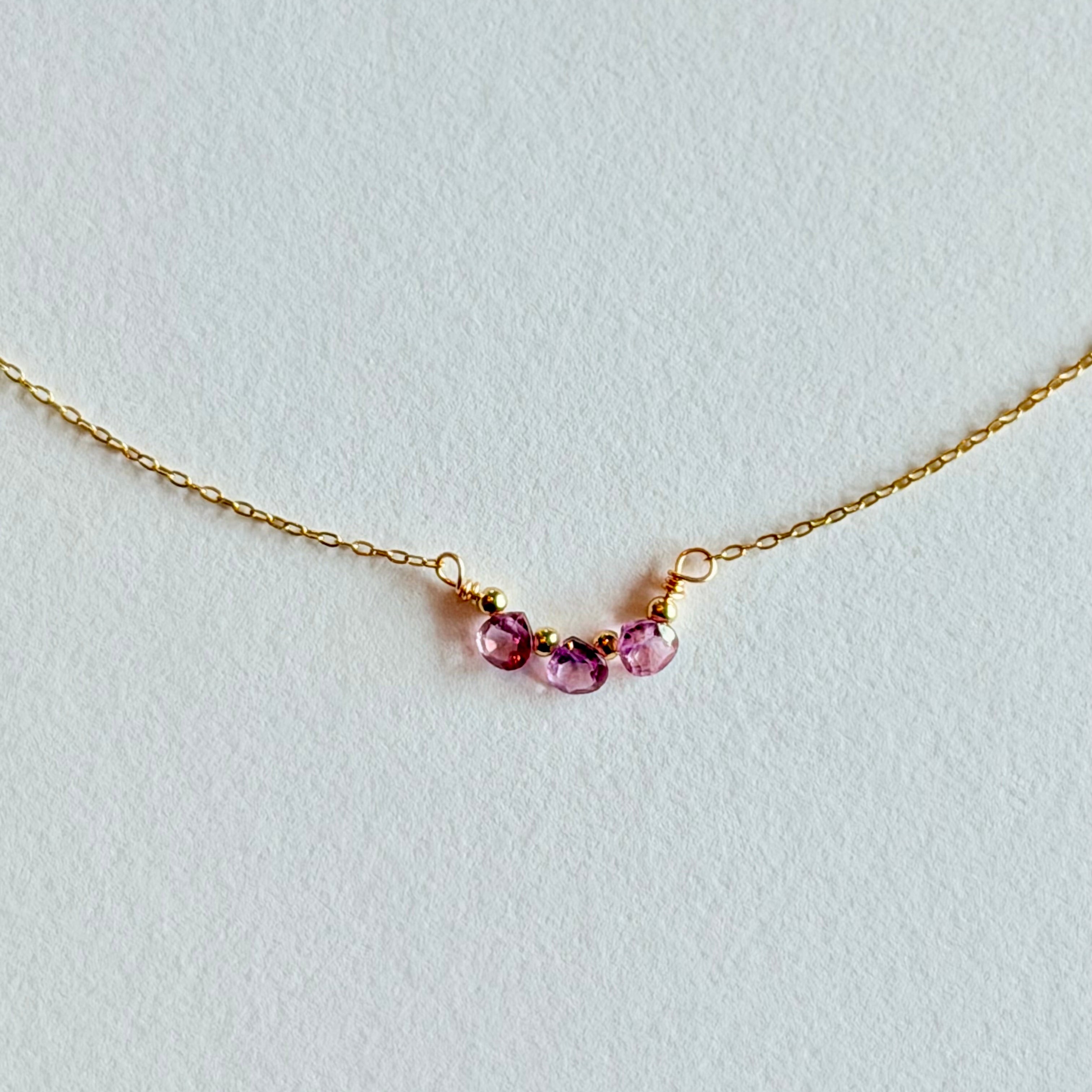 Delicate gold necklace with three small gemstones on a light gray background
