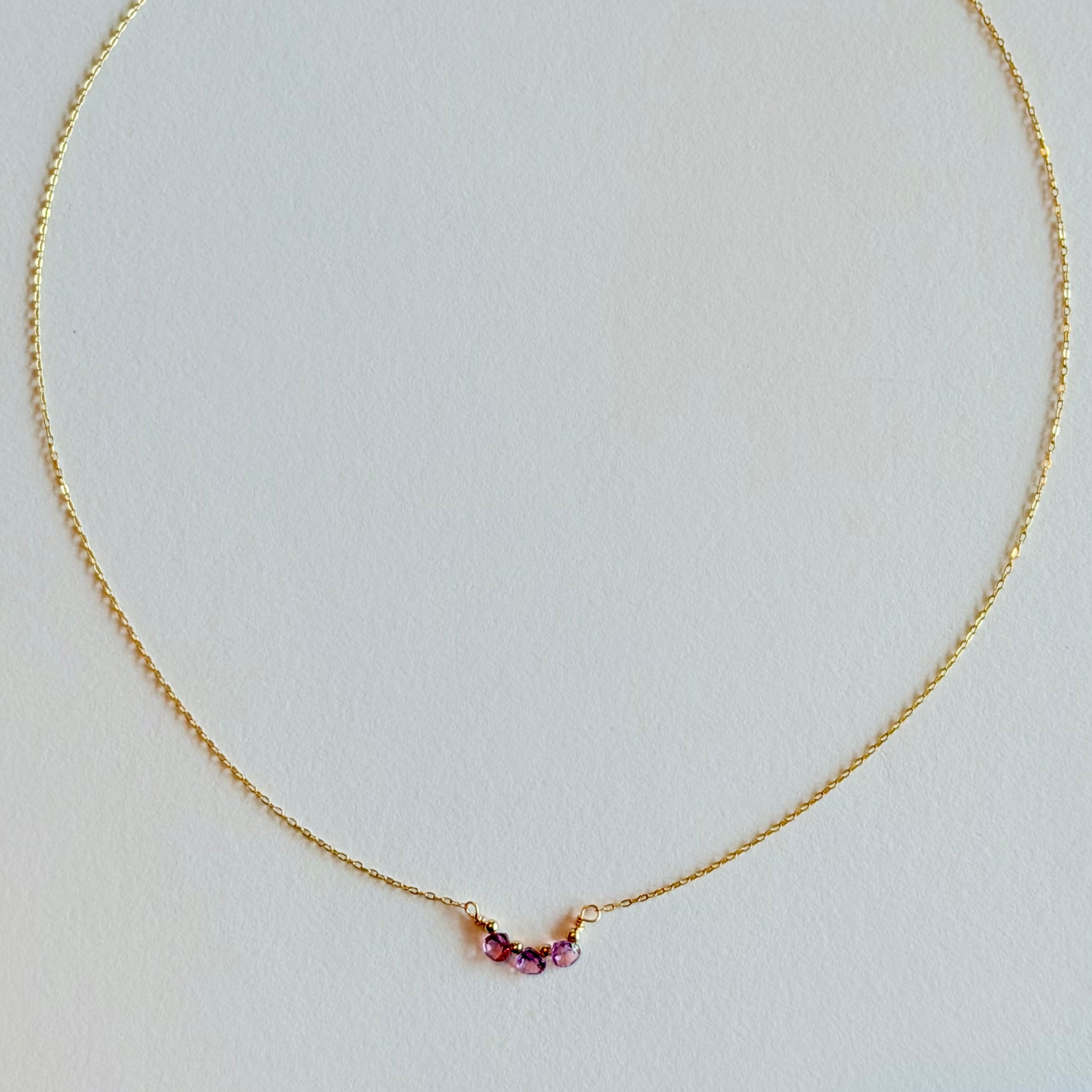 Gold necklace with small gemstones on a light gray background