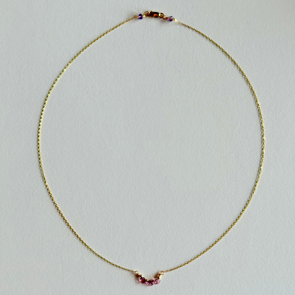 Gold necklace with small heart-shaped gemstones on a light gray background