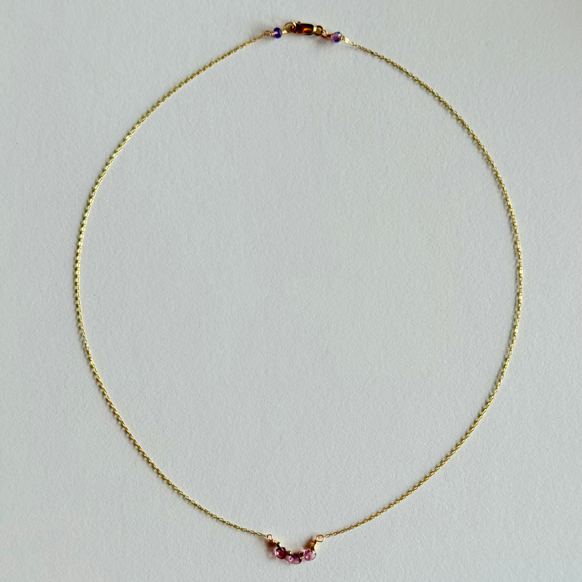 Gold necklace with small heart-shaped gemstones on a light gray background