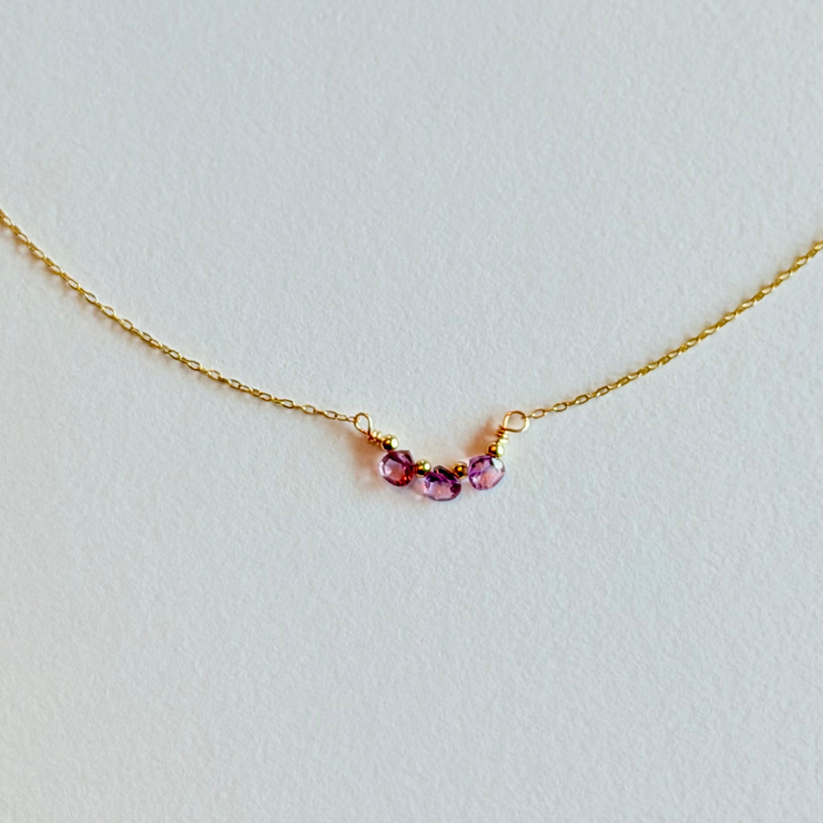 Gold necklace with three pink gemstones on a light gray background