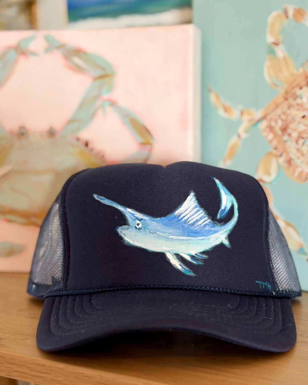 Navy blue trucker hat featuring an original hand-painted sailfish in shades of blue and white, coastal wearable art by Marie & Oakley.