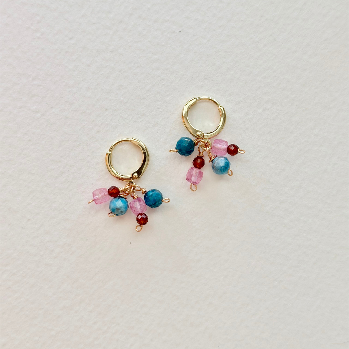 Gold hoop earrings with colorful beads on a light gray background