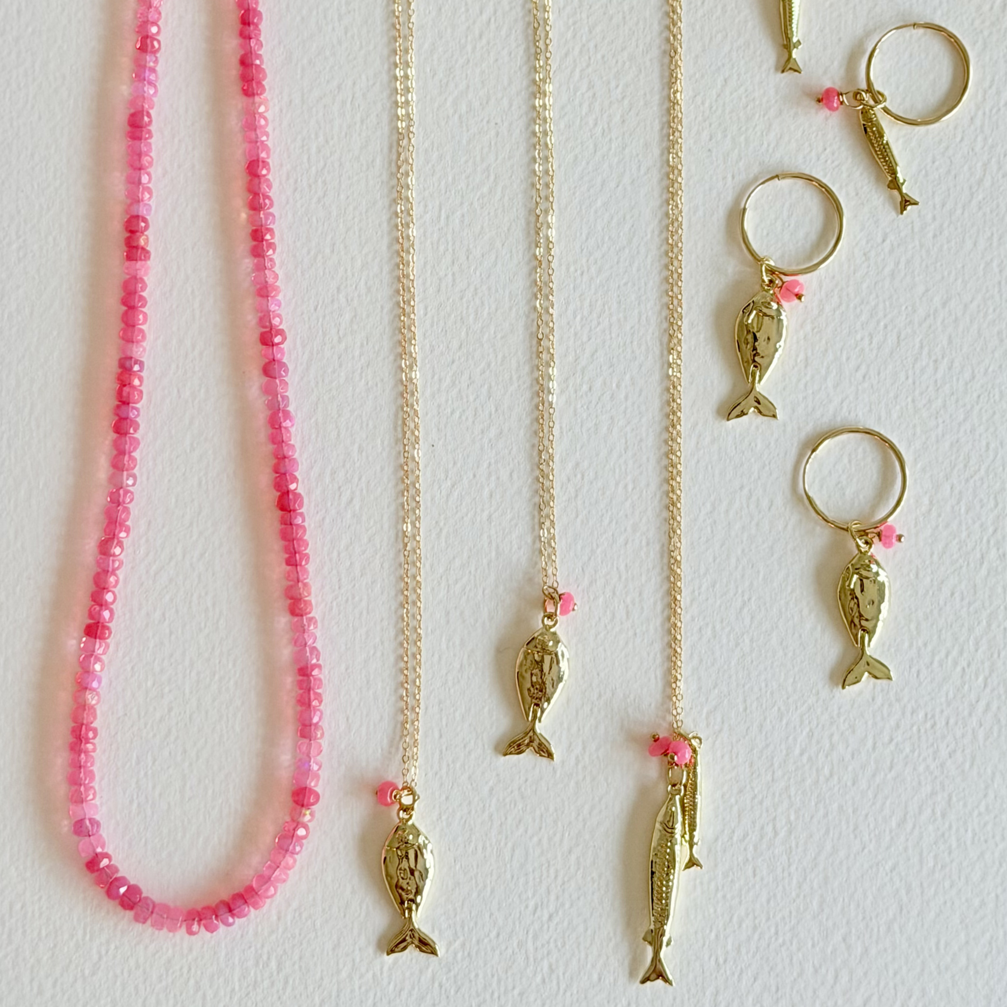 Gold necklaces with fish pendants and pink beads on a white background