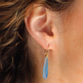Close-up of an ear wearing a blue teardrop earring with hair partially obscuring the view.