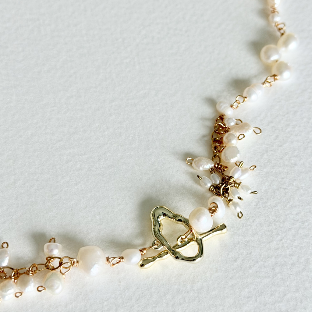 Pearl bracelet with gold clasp on a light gray background