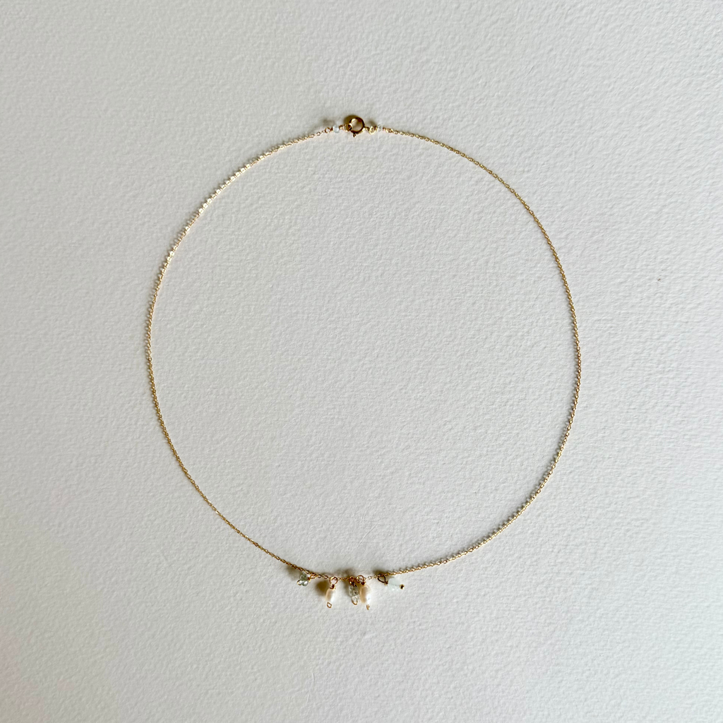 A delicate gold chain necklace with three small white shell charms, displayed on a textured off-white background.