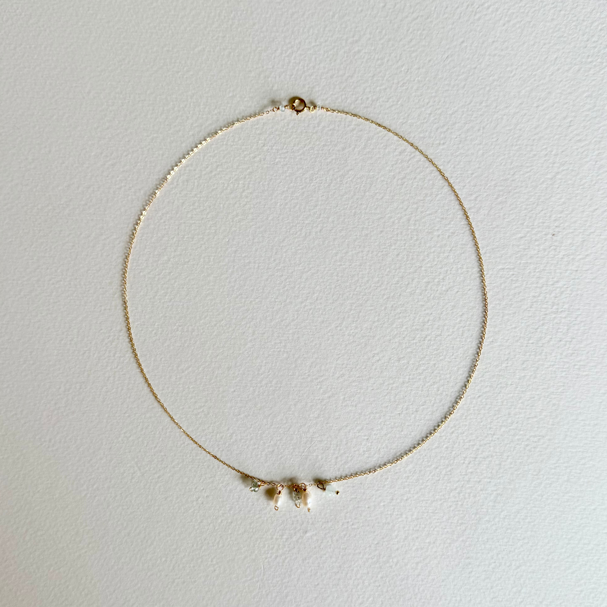 A delicate gold chain necklace with three small white shell charms, displayed on a textured off-white background.