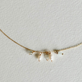 A delicate gold chain necklace featuring three small pearl-like bead drops and tiny clear crystal charms, displayed on a textured off-white background.