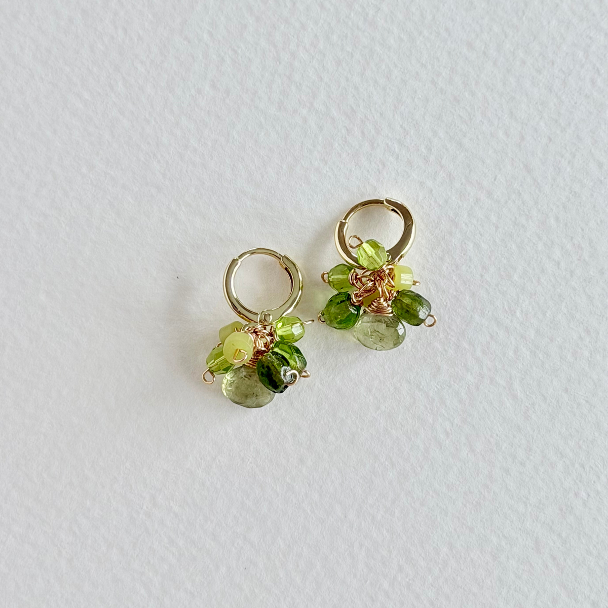 Pair of gold hoop earrings with green gemstones on a light gray background