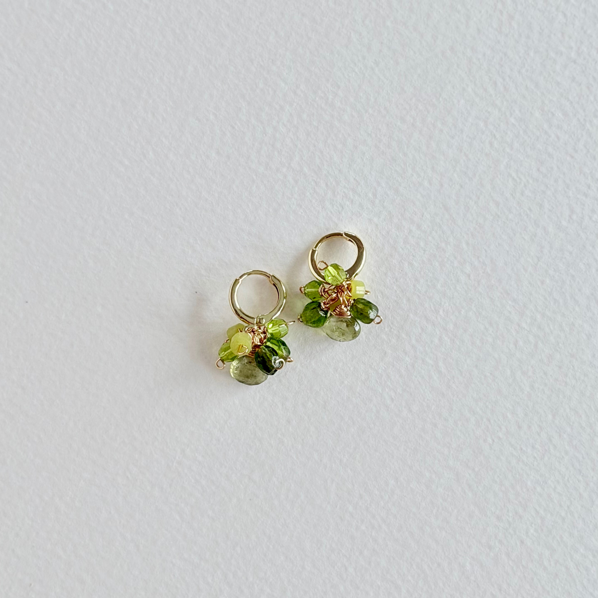 Pair of small green gemstone earrings on a light gray background