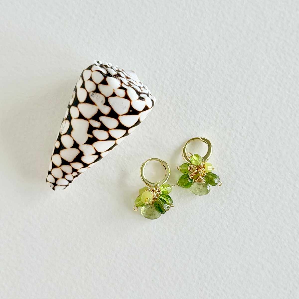 Pair of earrings with green gemstones on a white surface next to a shell.