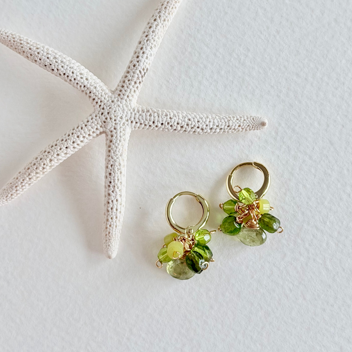 Green beaded earrings on a white surface with a starfish.
