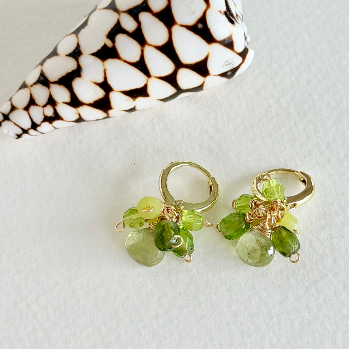 Gold earrings with green beads on a light background