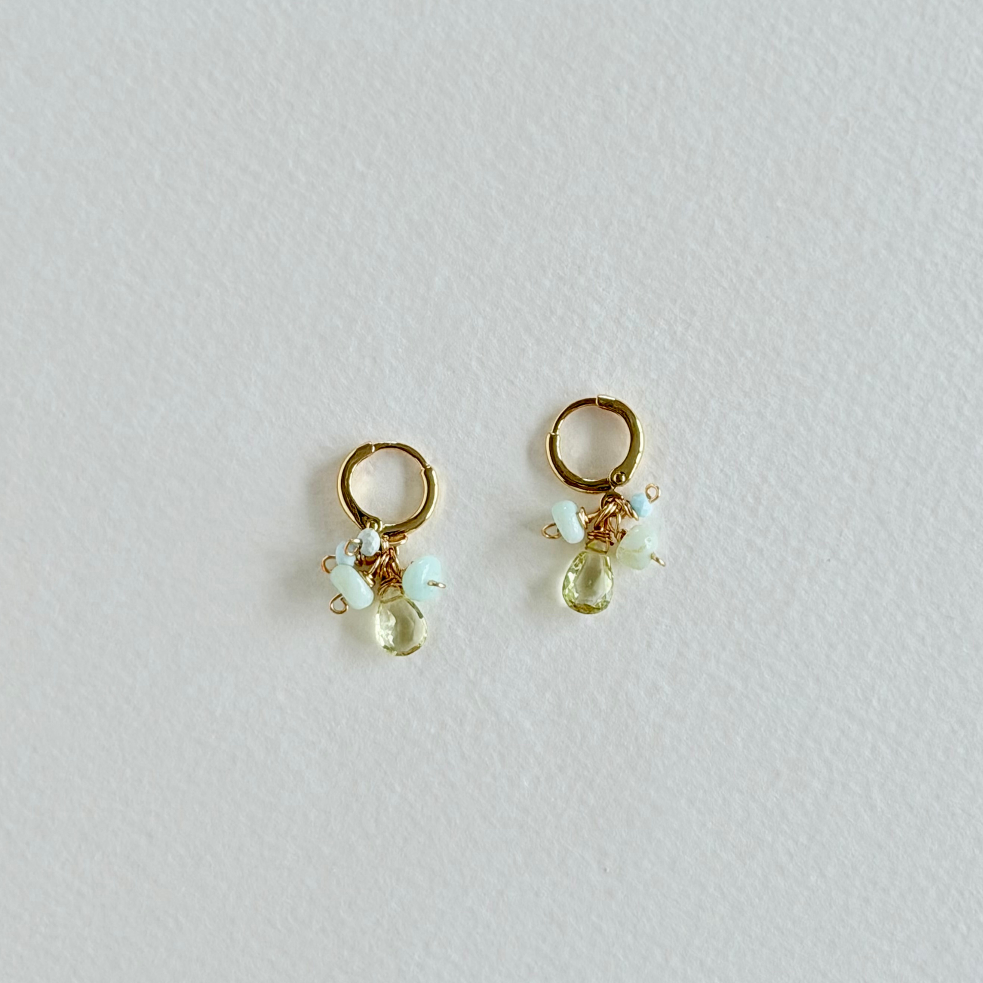 Gold earrings with green and clear gemstones on a light gray background