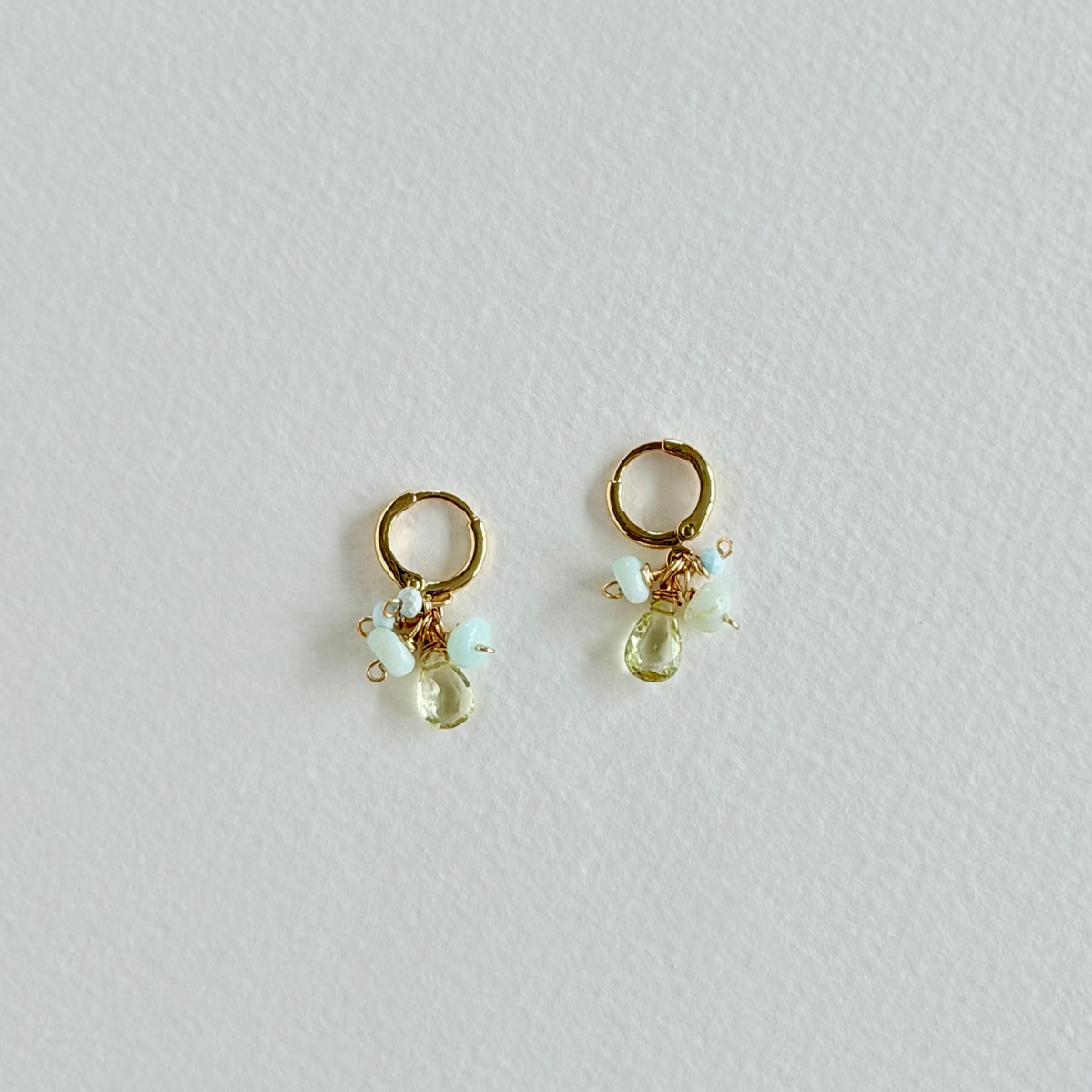 Gold earrings with green and clear gemstones on a light gray background