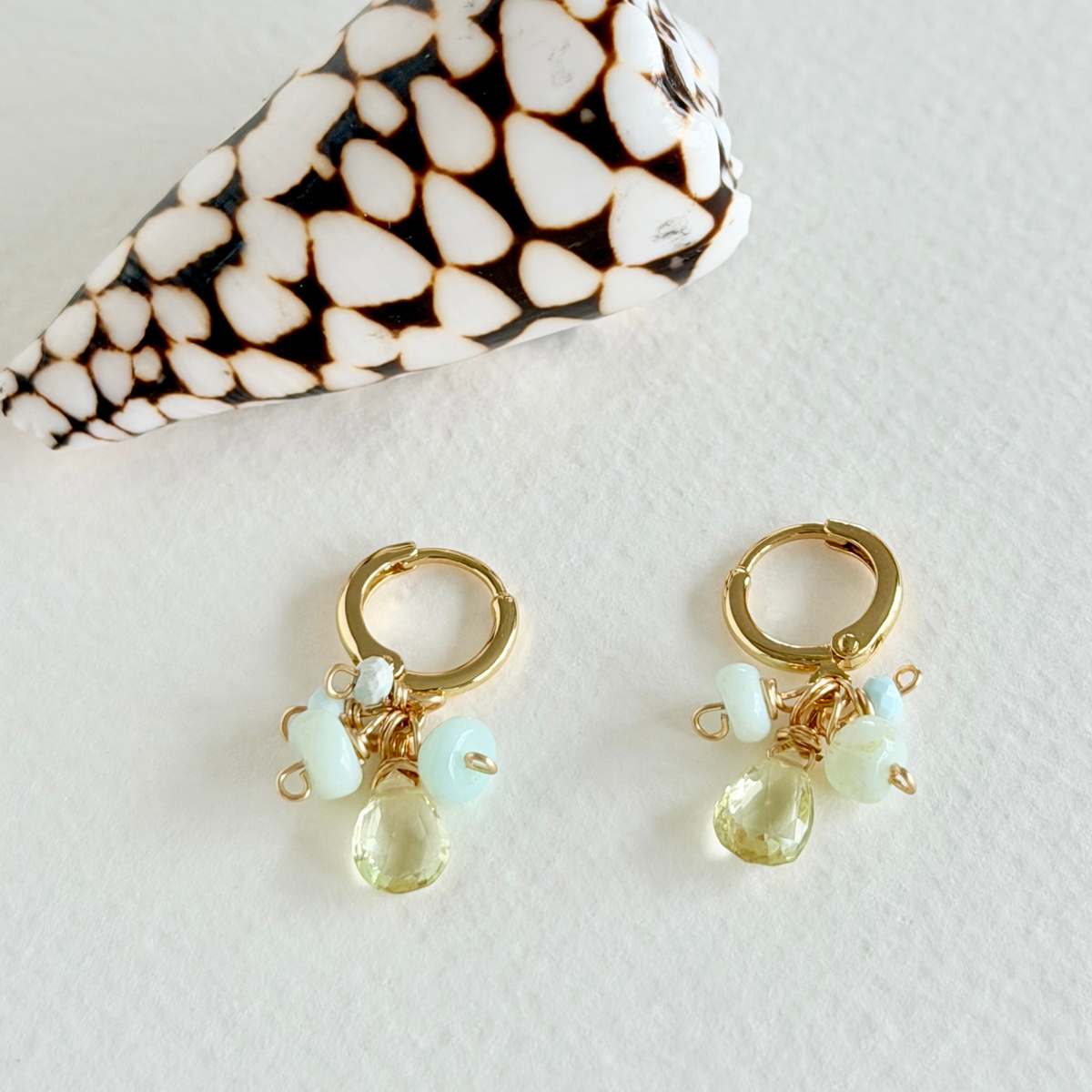 Gold hoop earrings with gemstone drops on a textured surface