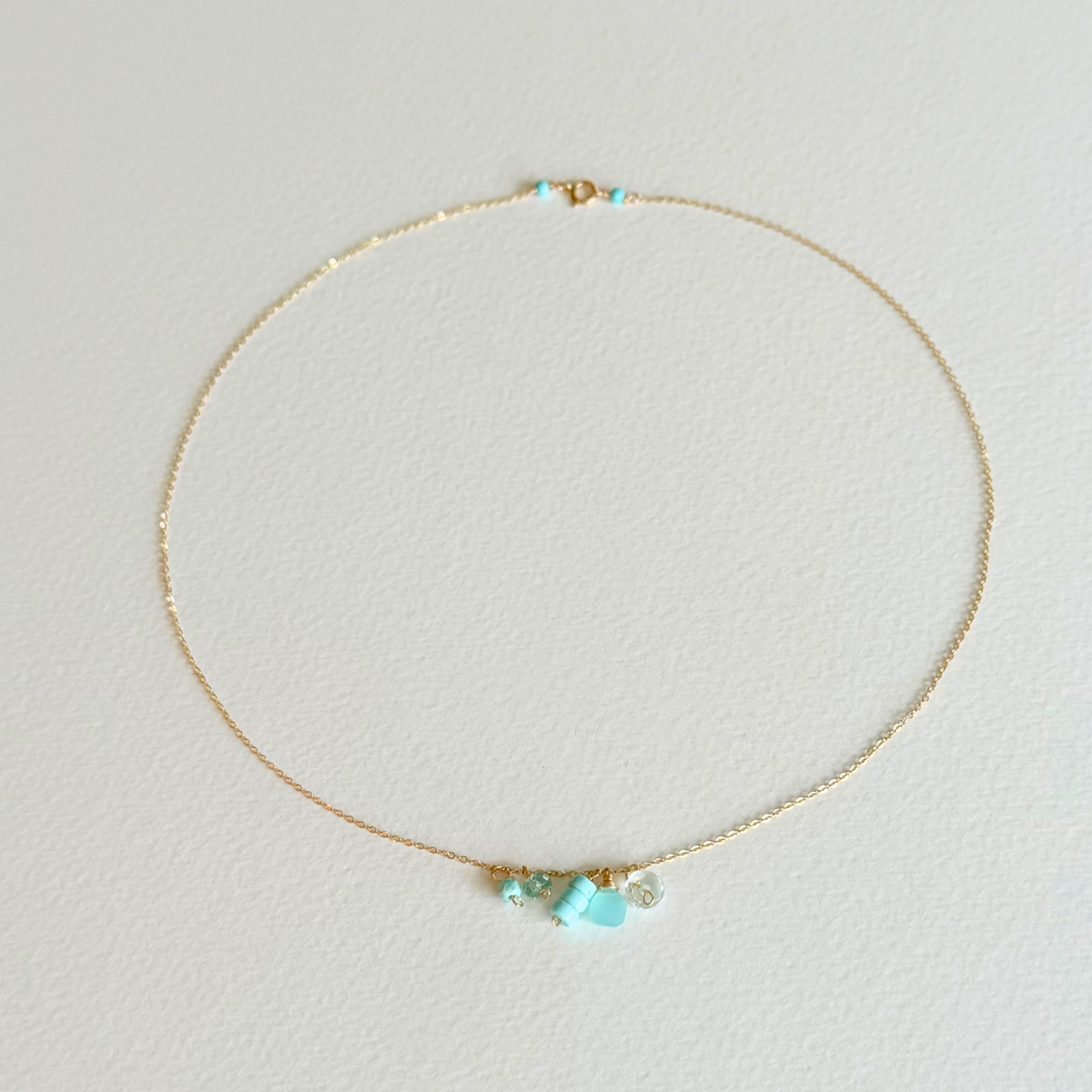 Delicate gold necklace with turquoise stones on a light gray background