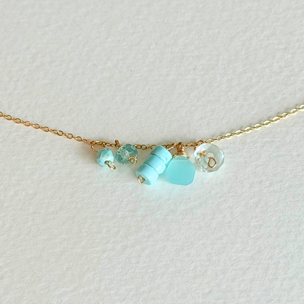 Delicate gold necklace with turquoise beads on a light background