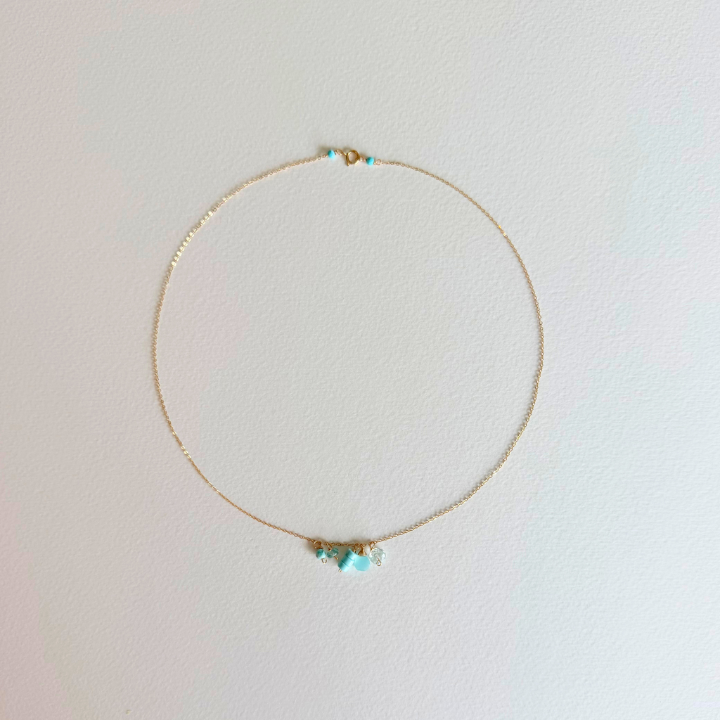 Delicate gold necklace with turquoise beads on a light pink background