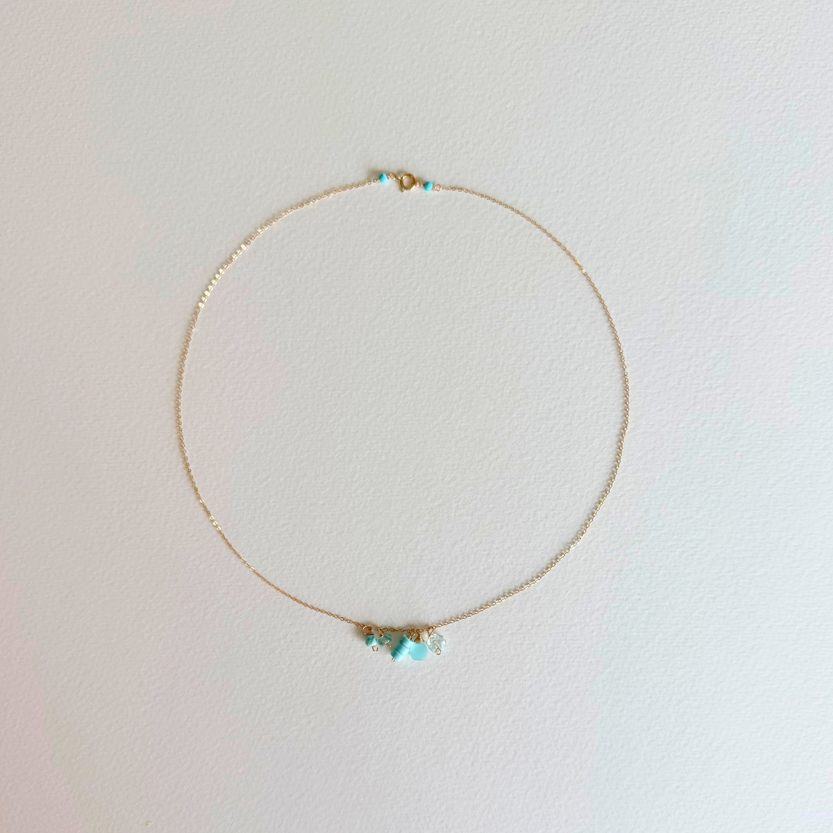 Delicate gold necklace with turquoise beads on a light pink background