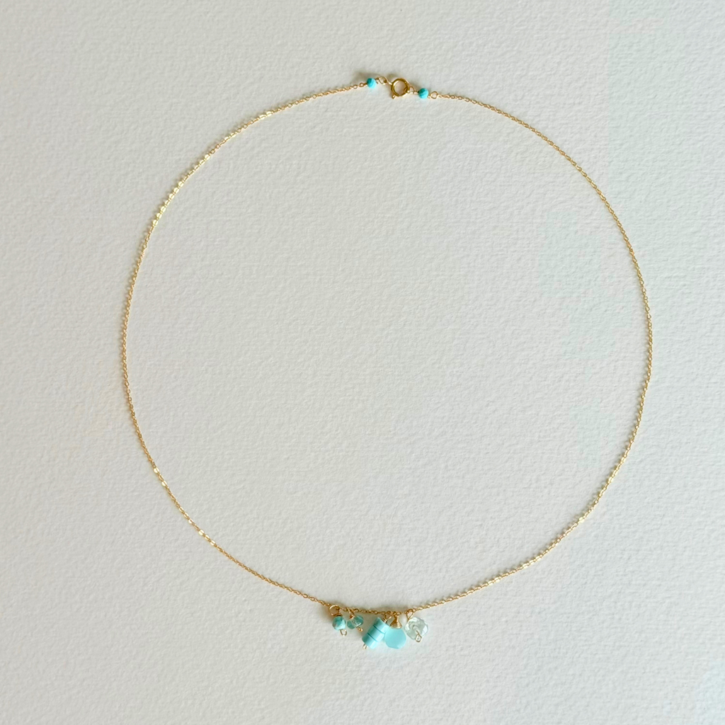 Delicate gold necklace with turquoise beads on a light gray background