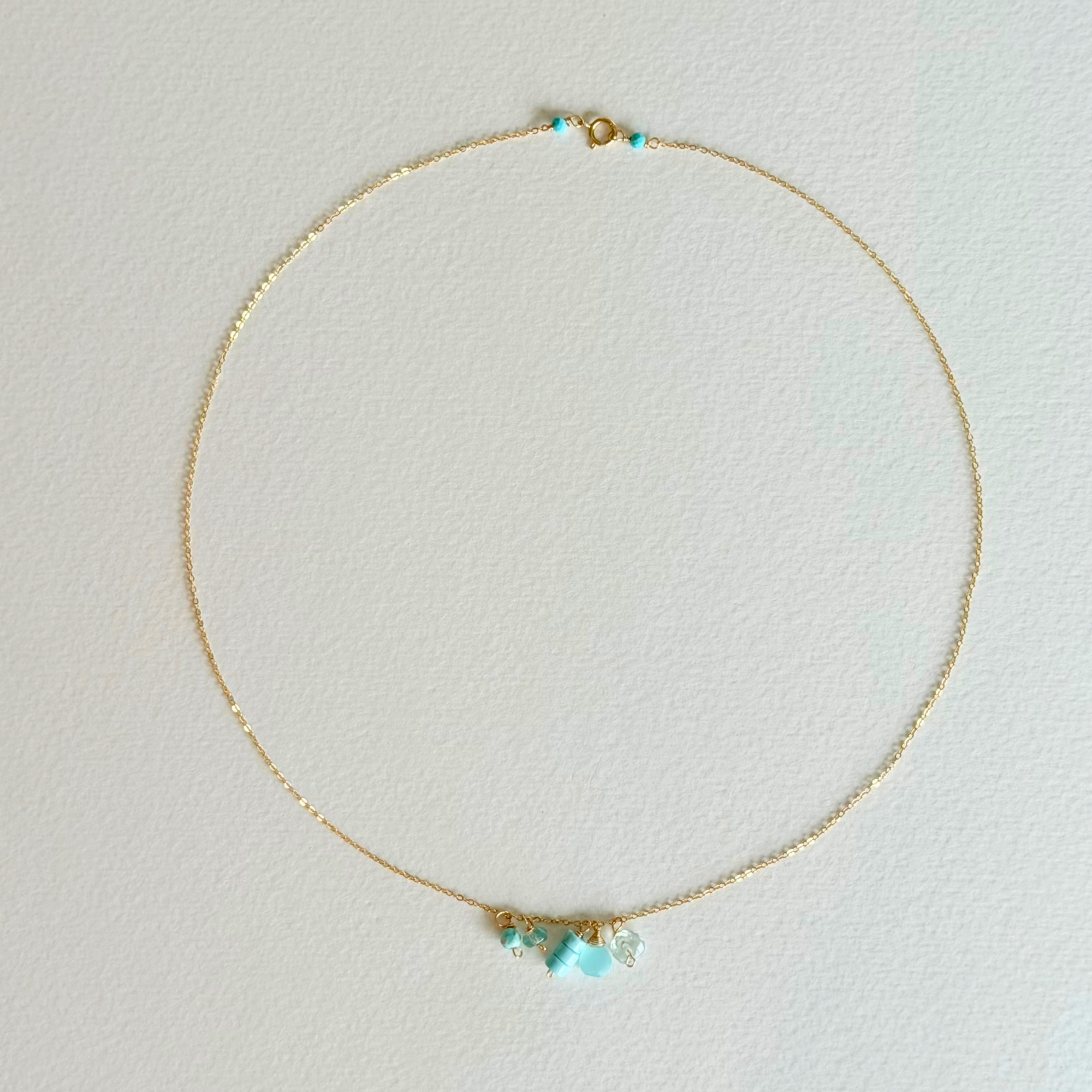 Delicate gold necklace with turquoise beads on a light gray background