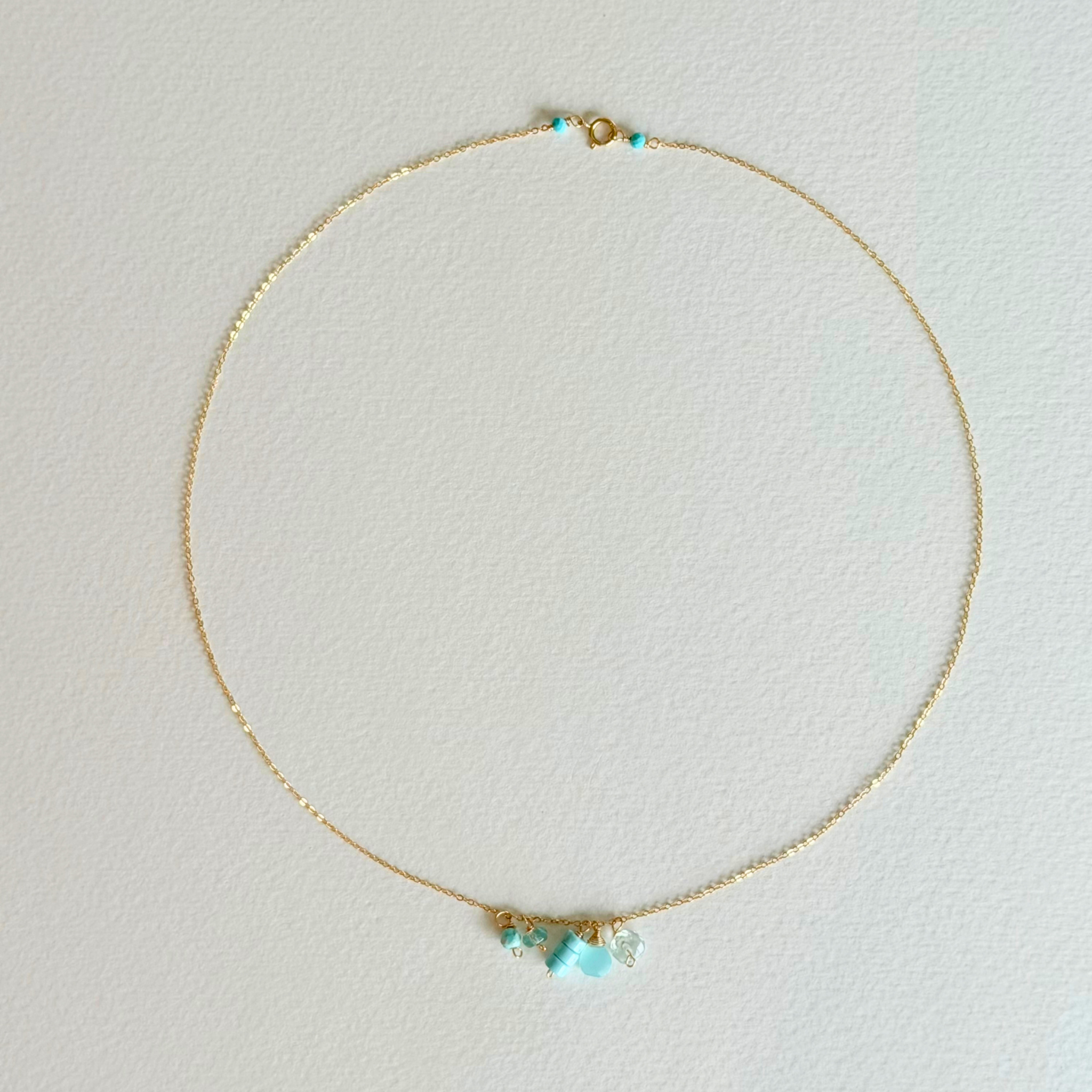 Delicate gold necklace with turquoise beads on a light gray background