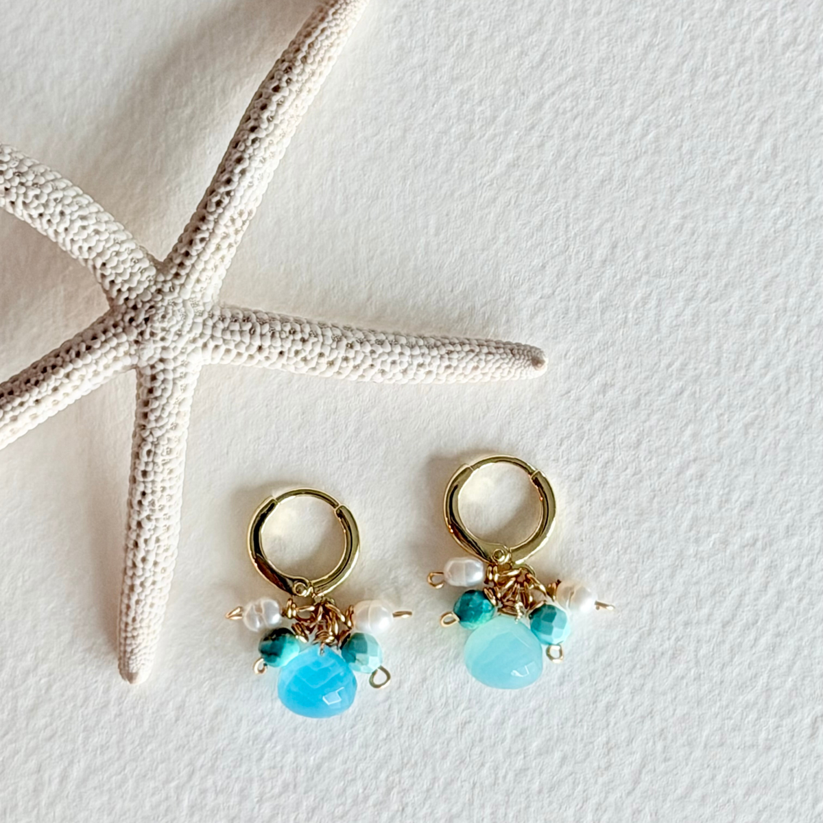 Gold hoop earrings with turquoise and pearl beads on a white background with a starfish.