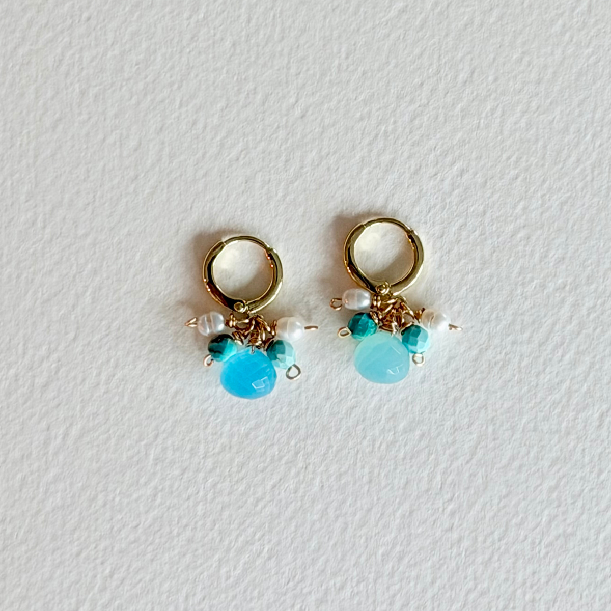 Pair of gold earrings with turquoise beads and pearls on a light gray background