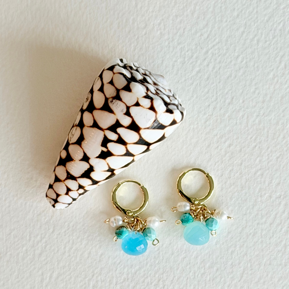 Pair of earrings with turquoise beads and gold hooks next to a shell on a light background