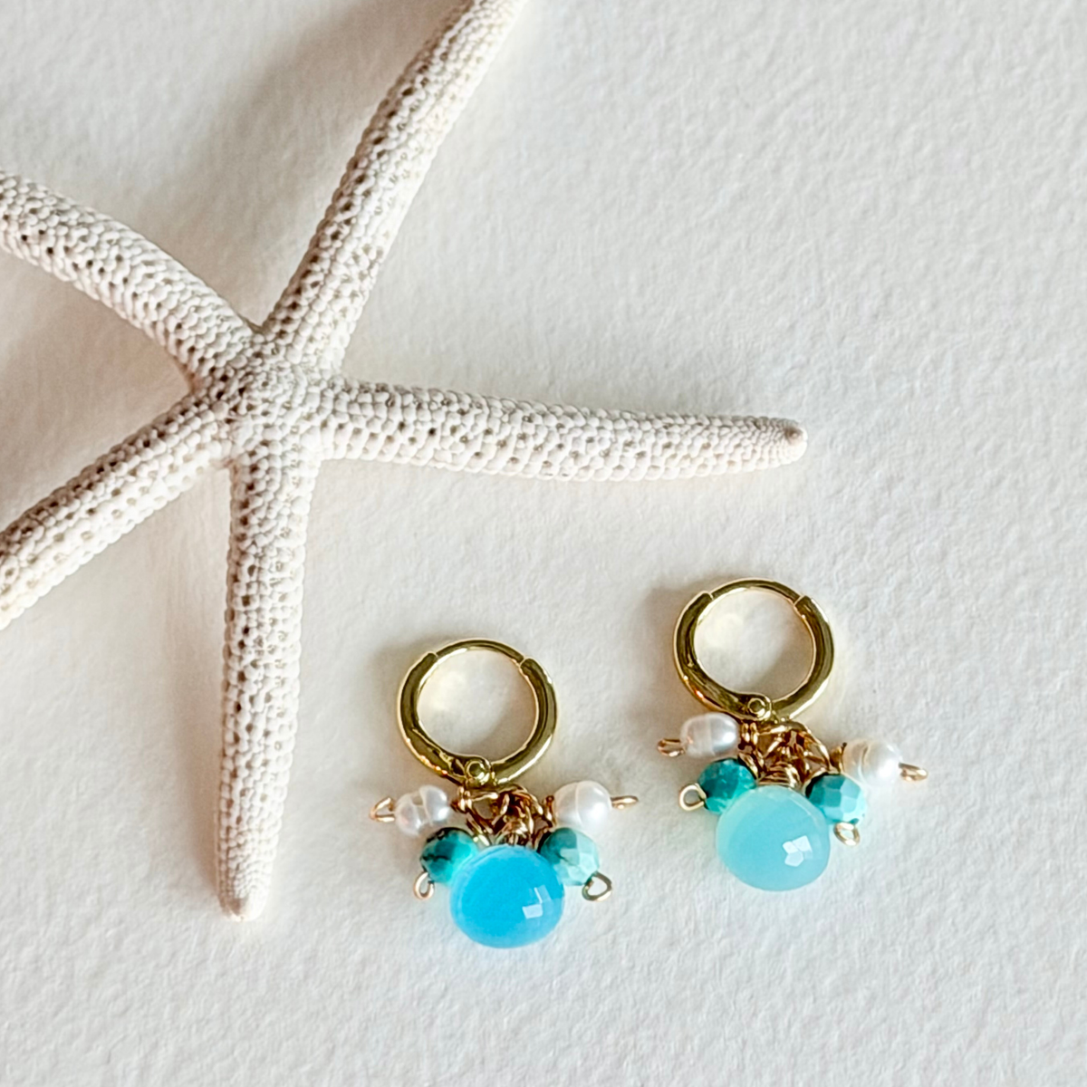 Gold hoop earrings with turquoise beads and pearls on a white background with a starfish.