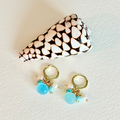Pair of gold earrings with turquoise beads and pearls on a textured white surface.