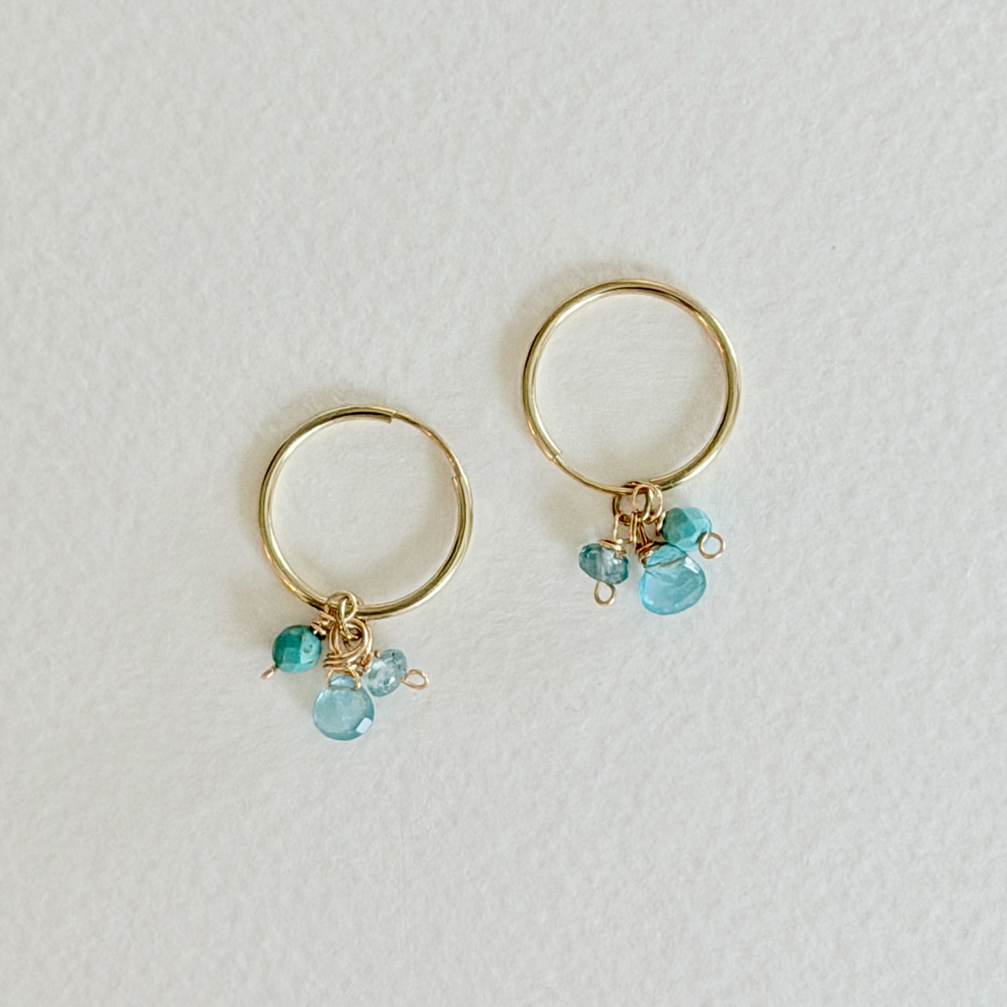 Gold hoop earrings with turquoise beads on a light gray background