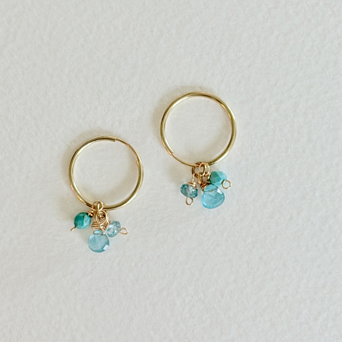 Gold hoop earrings with turquoise gemstones on a light gray background
