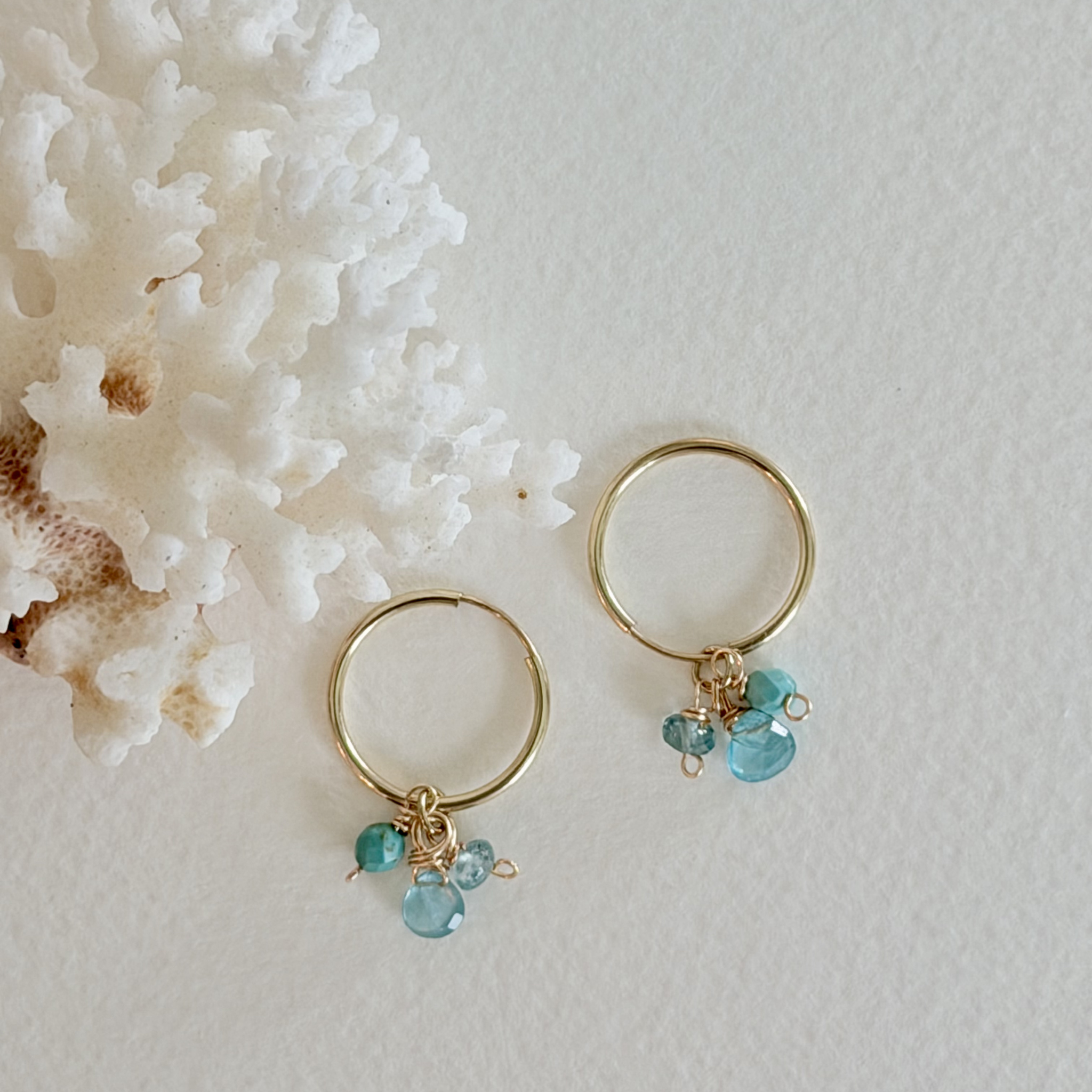 Gold hoop earrings with turquoise beads on a light gray background