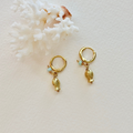 Gold hoop earrings with fish charms on a white coral background