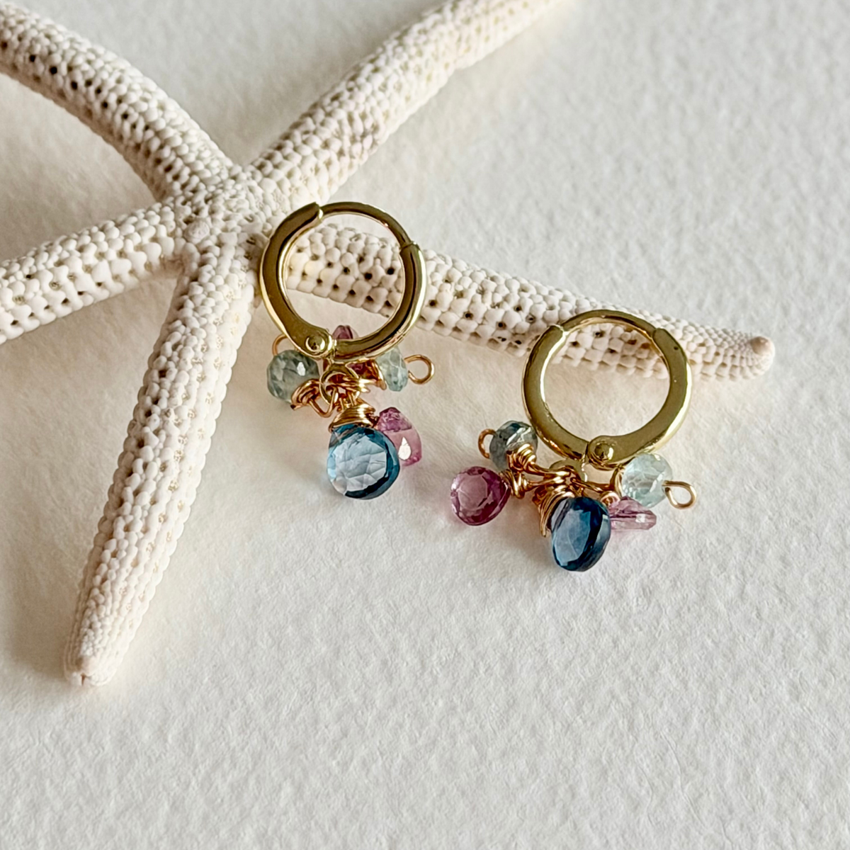 Gold hoop earrings with colorful beads on a starfish and shell background