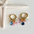 Gold hoop earrings with colorful beads on a textured white surface with a starfish.