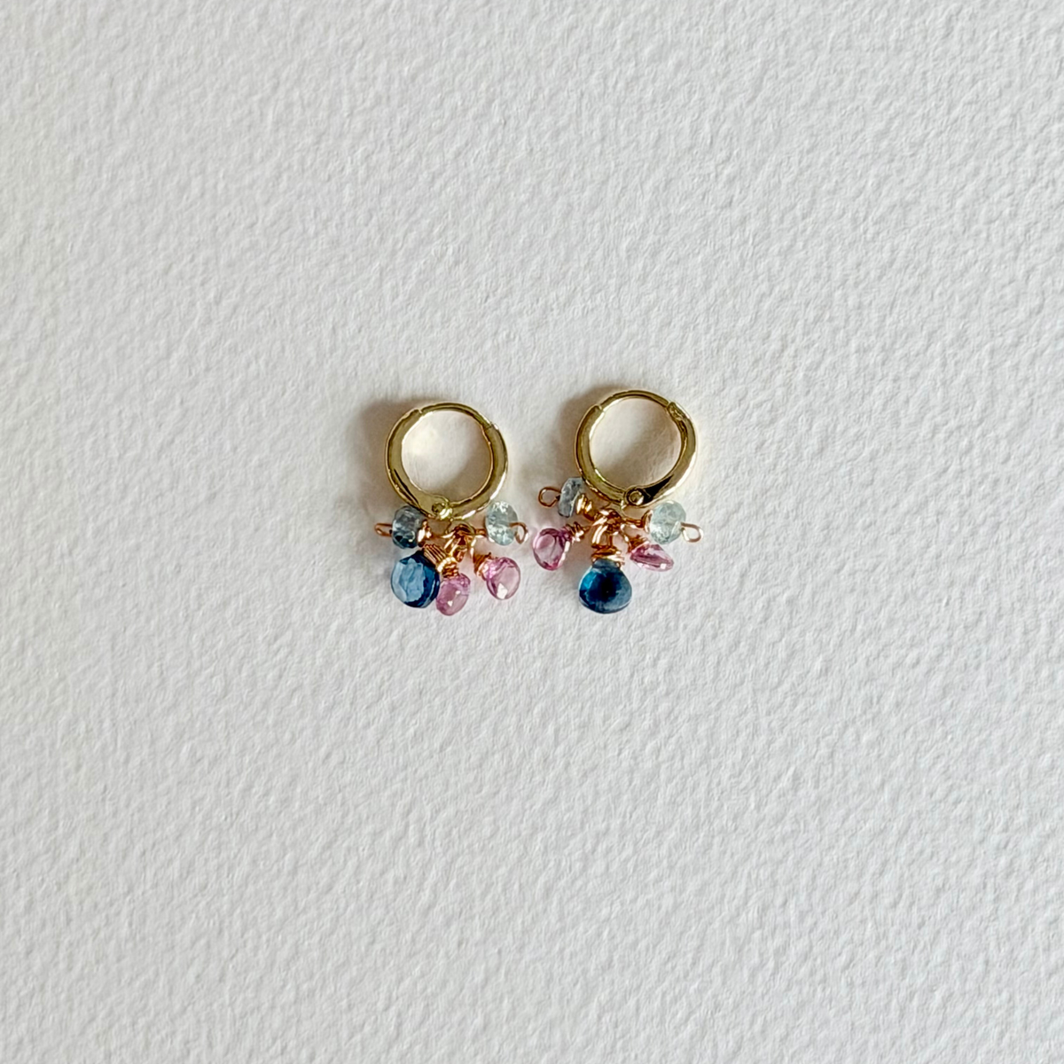 Gold hoop earrings with colorful gemstones on a light gray background