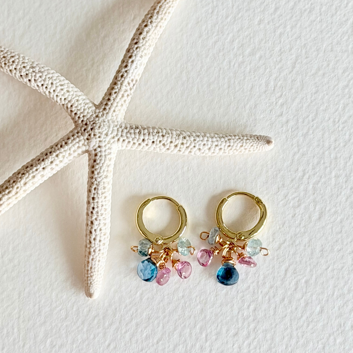 Gold hoop earrings with colorful beads on a white surface with a starfish.