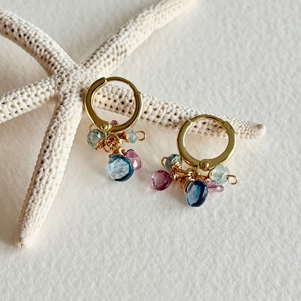 Gold hoop earrings with colorful beads on a starfish and sand background