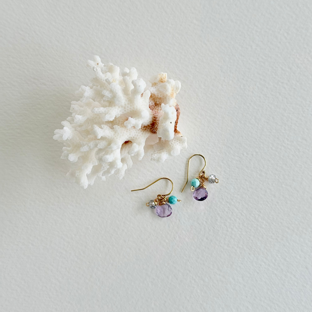 Gold earrings with gemstones on a white surface with coral