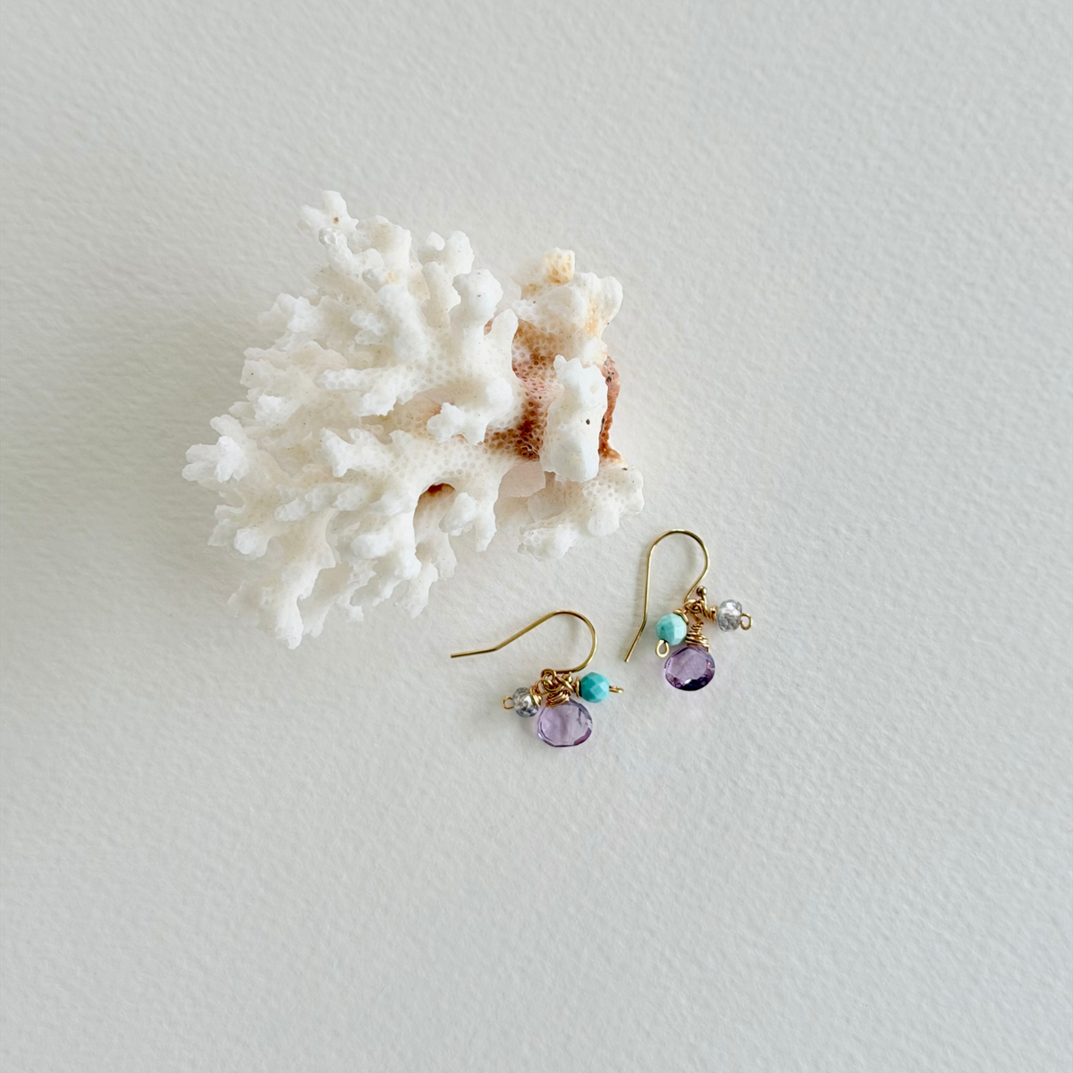 Gold earrings with gemstones on a white surface with coral