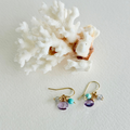 Pair of gold earrings with purple and turquoise beads on a white surface with coral.