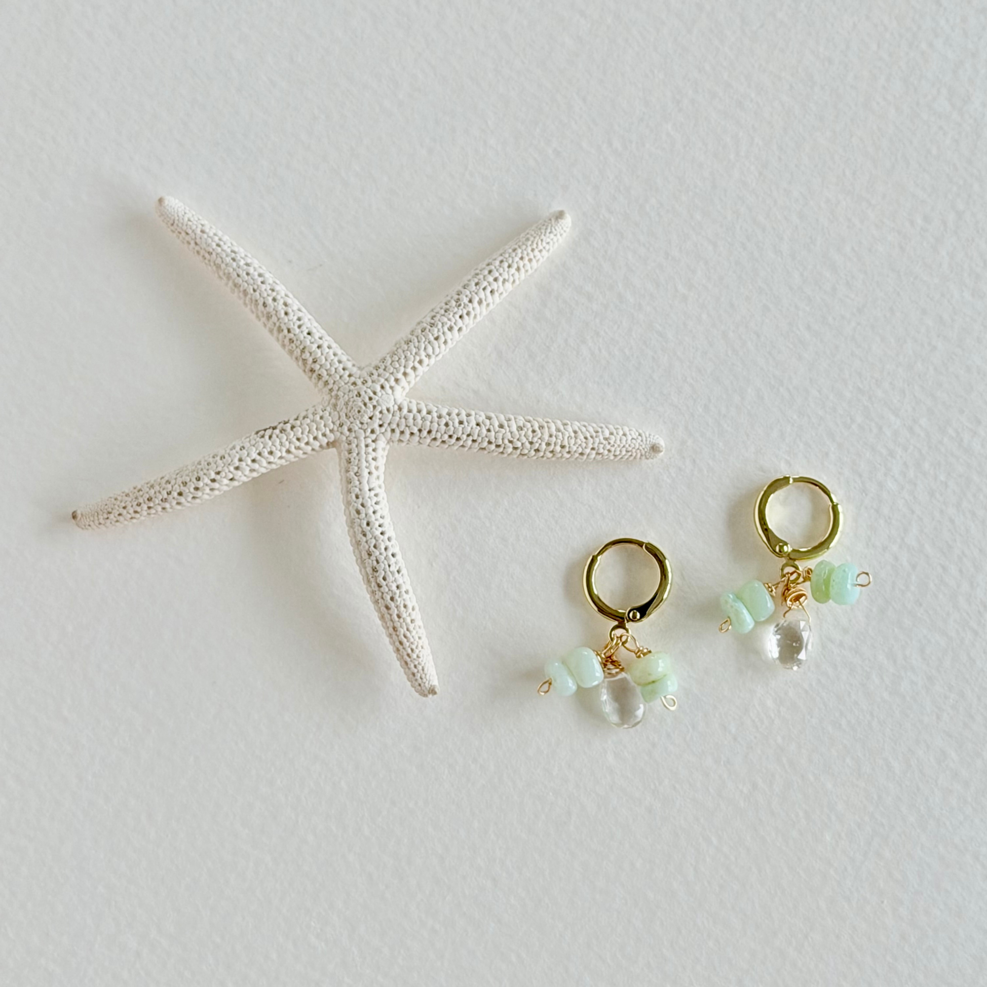 Pair of gold earrings with green beads on a white surface with a starfish.